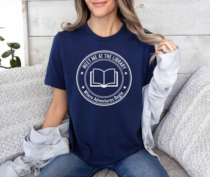 A comfort colors® shirt with the saying "meet me at the library where adventures begin"