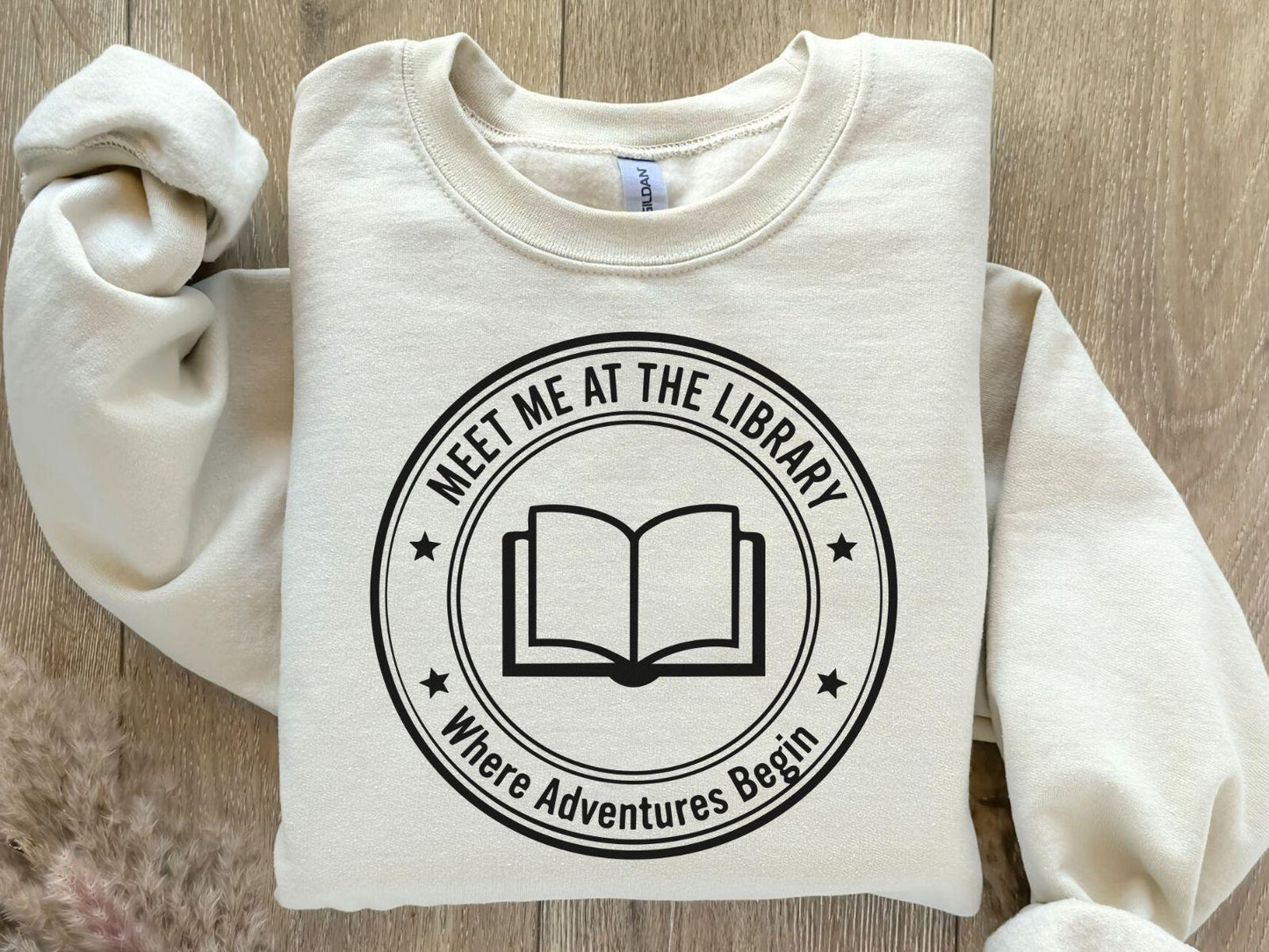 A Gildan 18000 sweatshirt with the saying "meet me at the library where adventures begin"