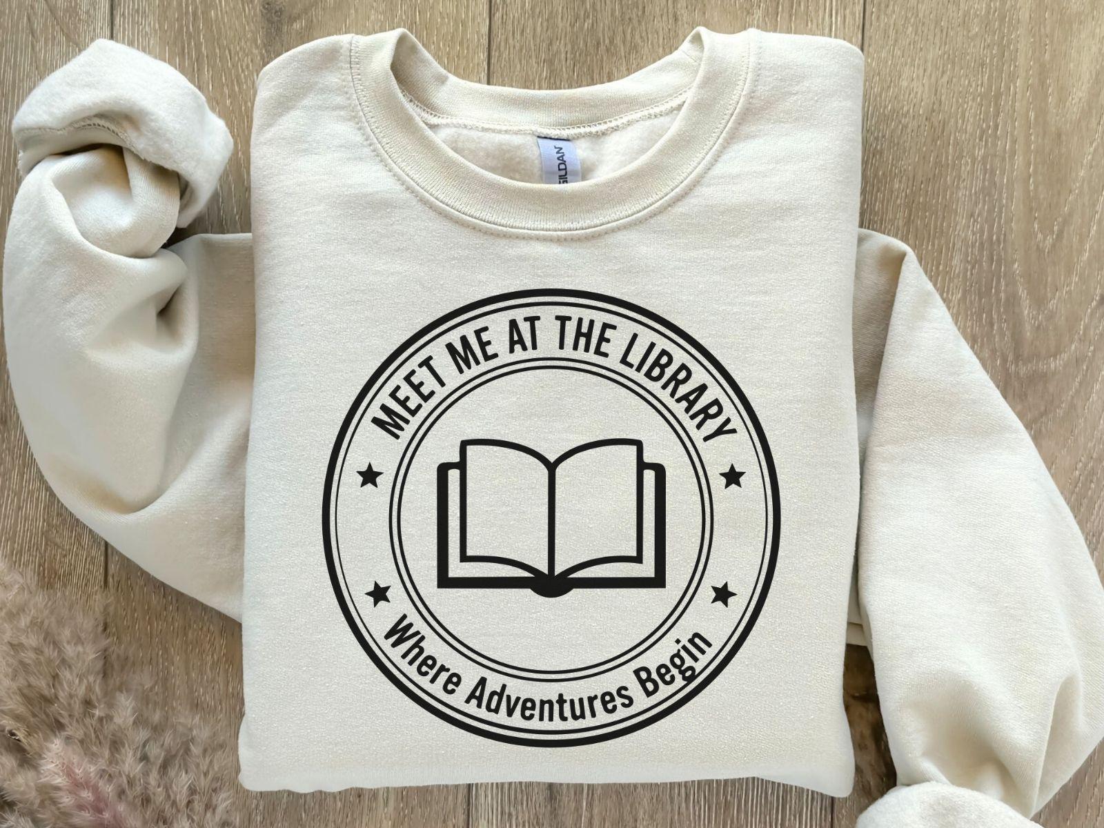 A Gildan 18000 sweatshirt with the saying "meet me at the library where adventures begin"