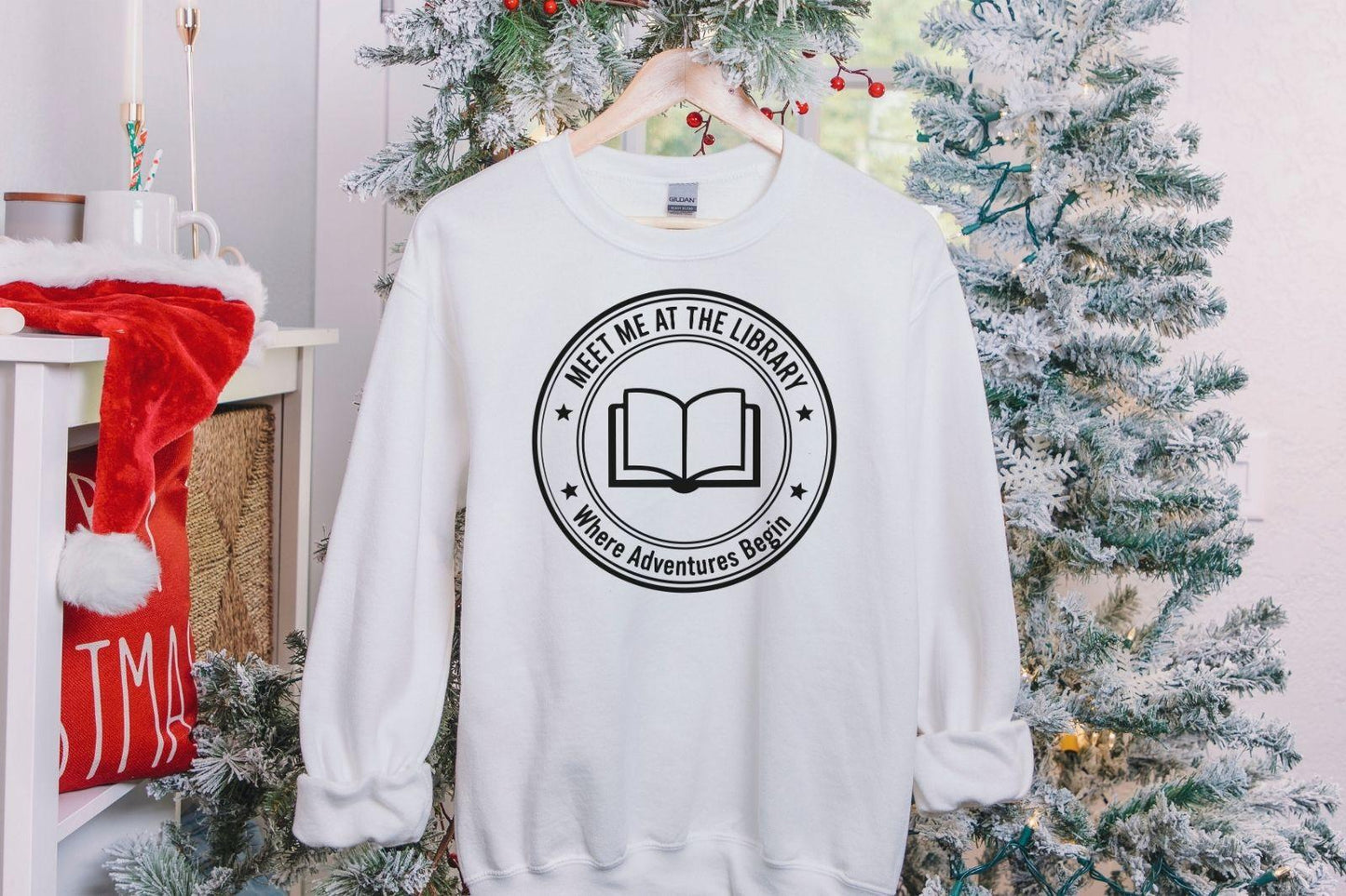 A Gildan 18000 sweatshirt with the saying "meet me at the library where adventures begin"