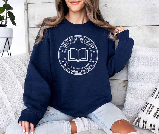 A Gildan 18000 sweatshirt with the saying "meet me at the library where adventures begin"