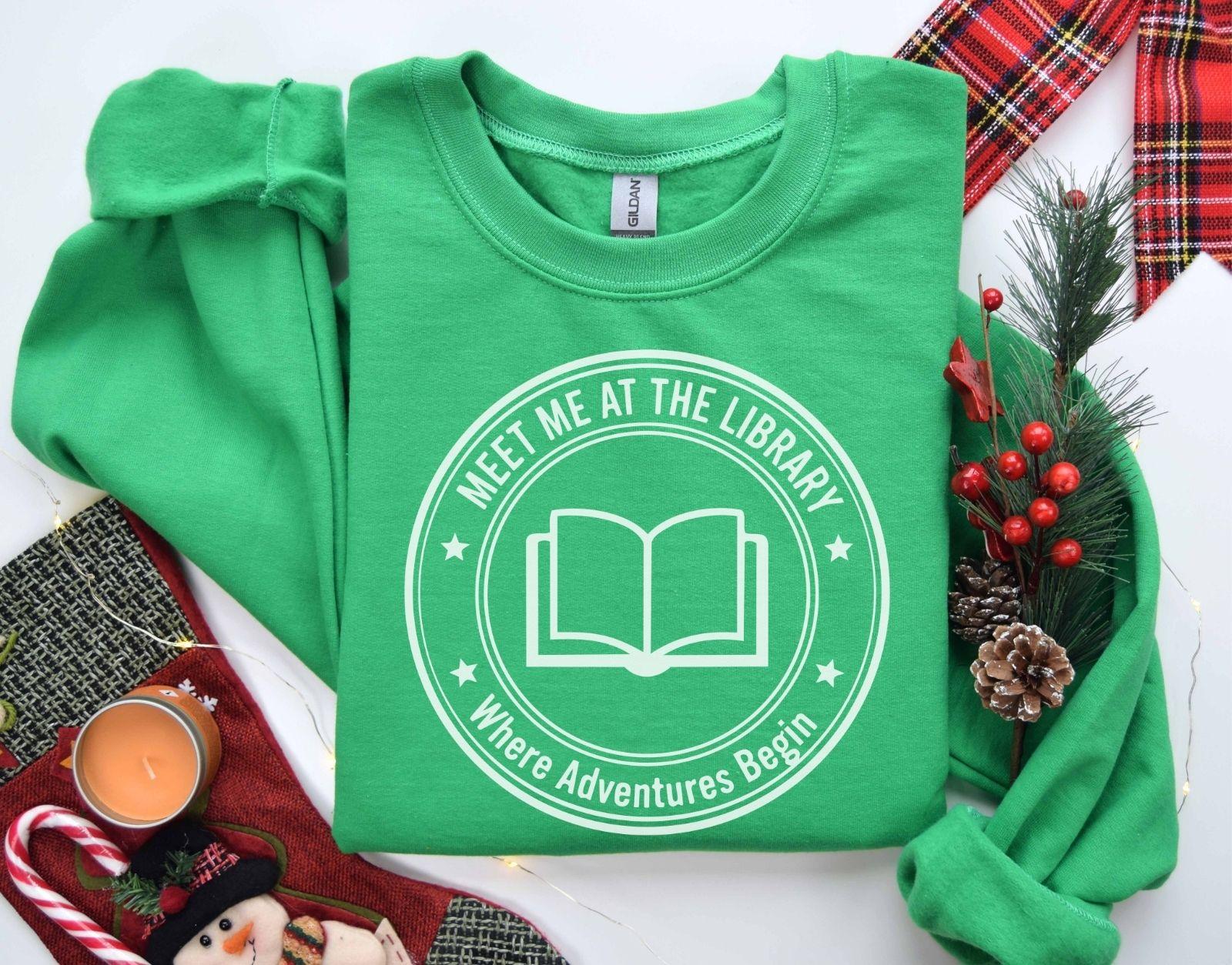 A Gildan 18000 sweatshirt with the saying "meet me at the library where adventures begin"