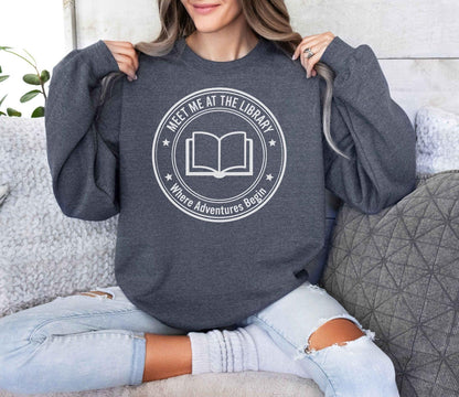 A Gildan 18000 sweatshirt with the saying "meet me at the library where adventures begin"