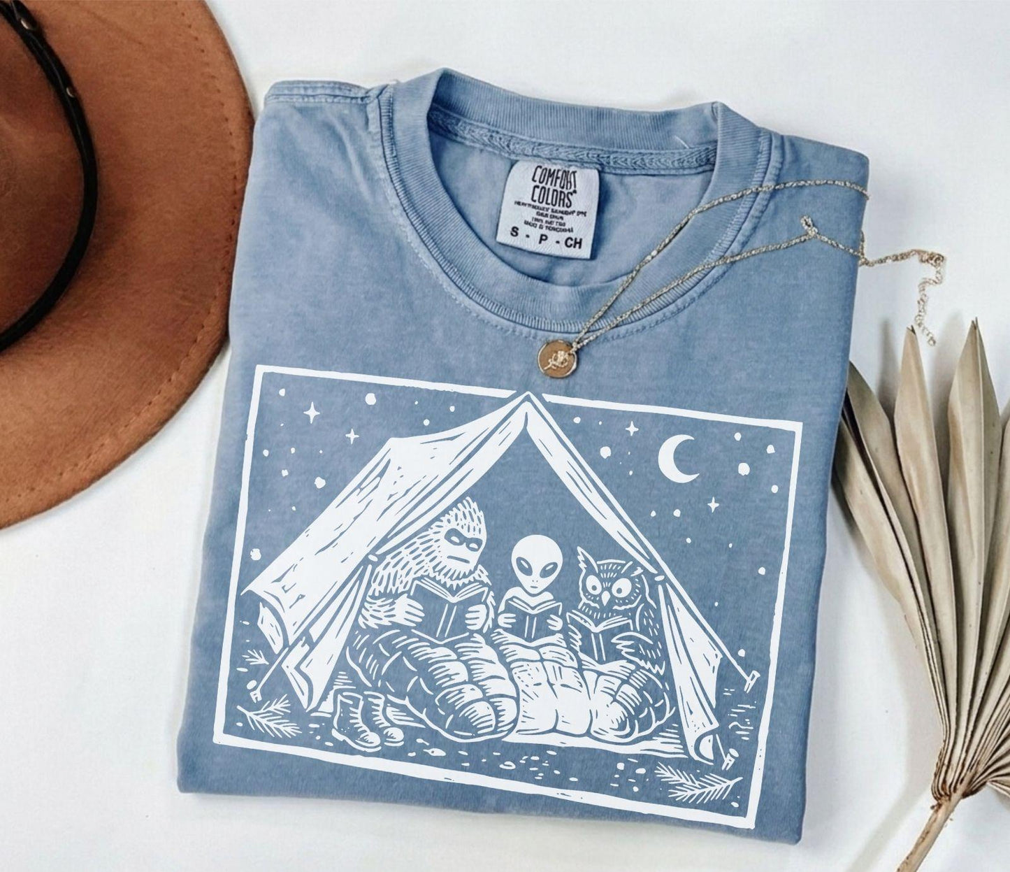 A comfort colors® shirt with the saying "Mothman Bigfoot and Horned reading a book"