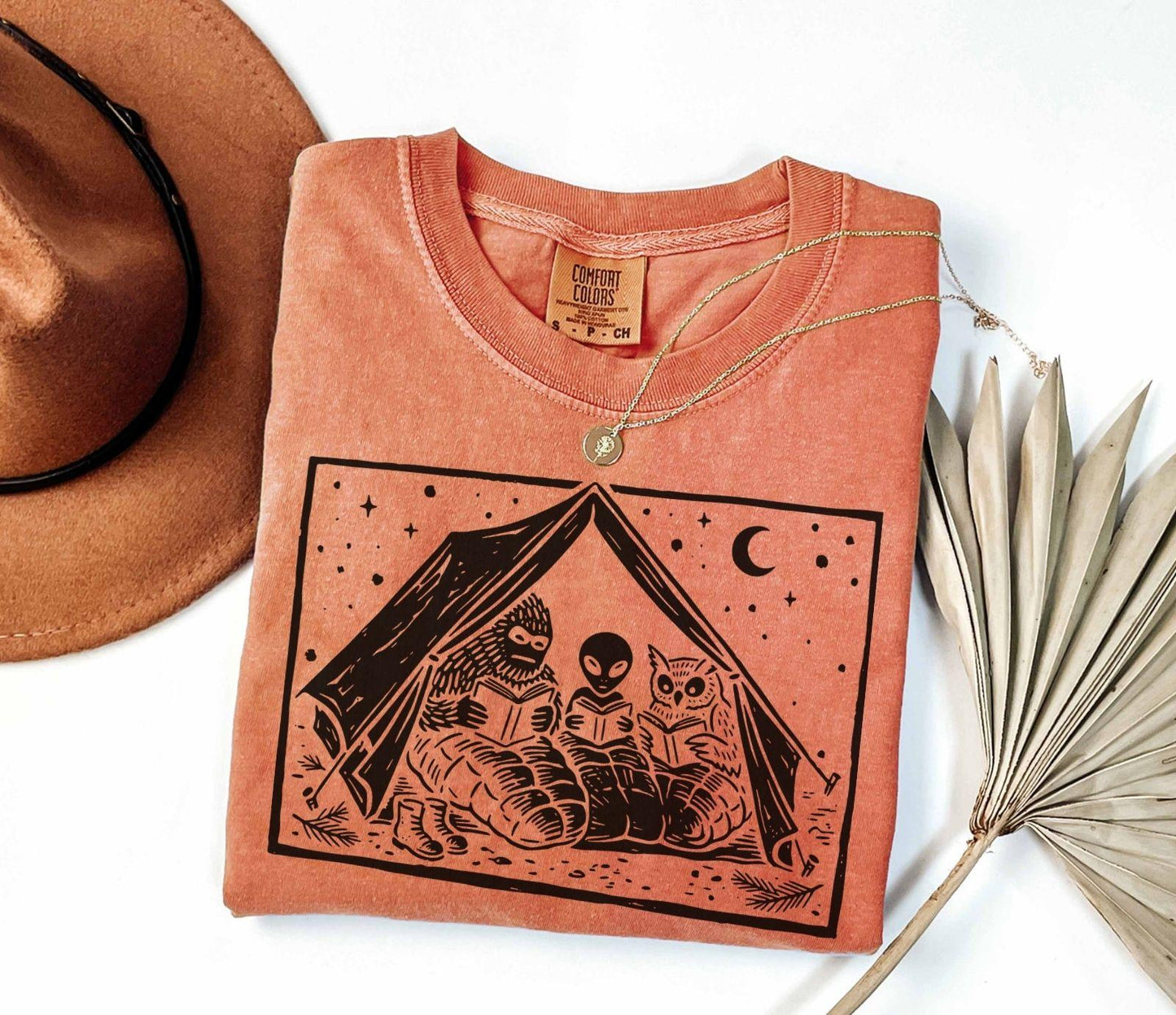 A comfort colors® shirt with the saying "Mothman Bigfoot and Horned reading a book"