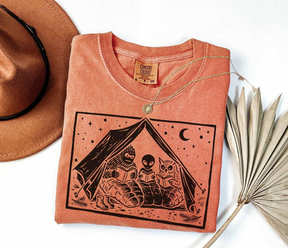 A comfort colors® shirt with the saying "Mothman Bigfoot and Horned reading a book"