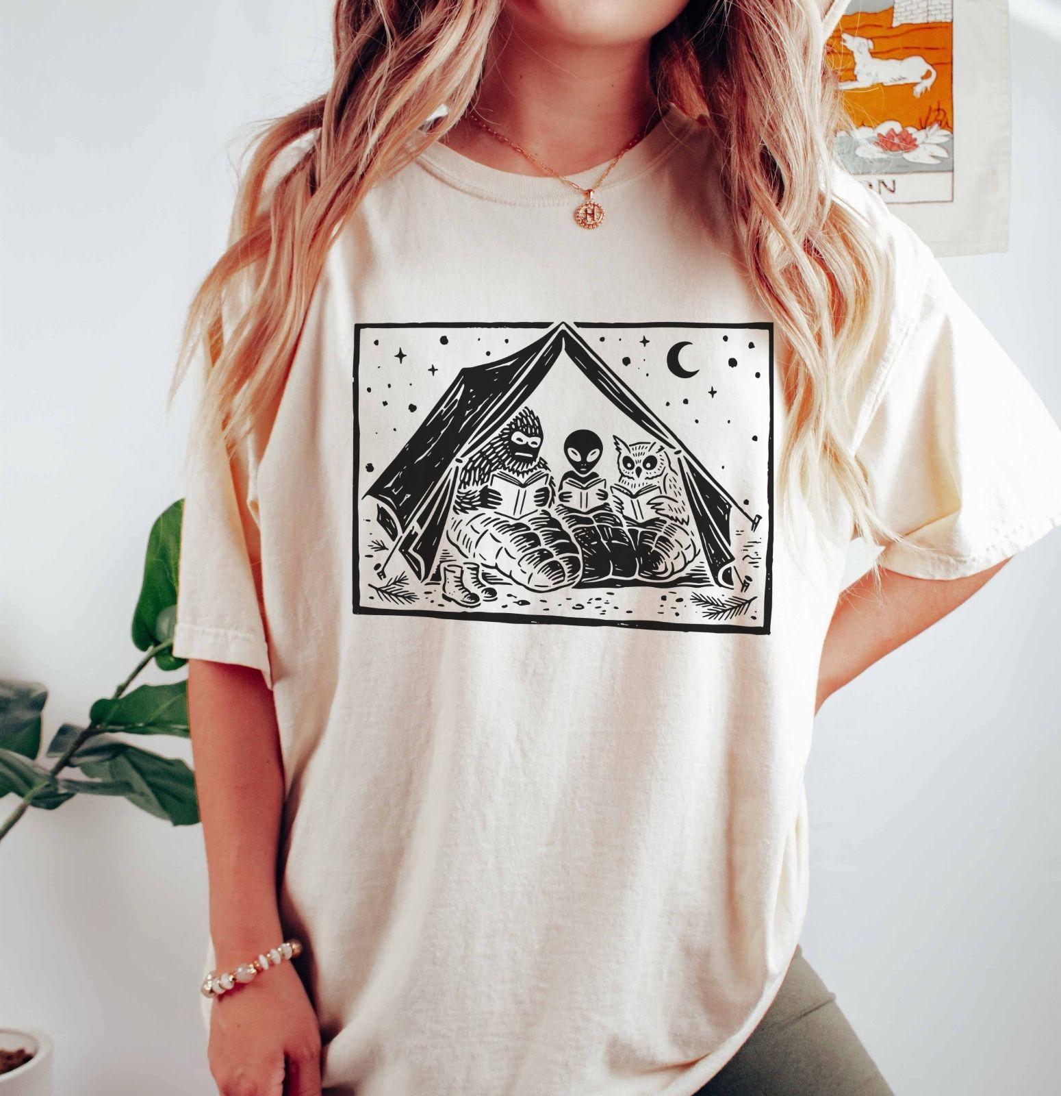 A comfort colors® shirt with the saying "Mothman Bigfoot and Horned reading a book"