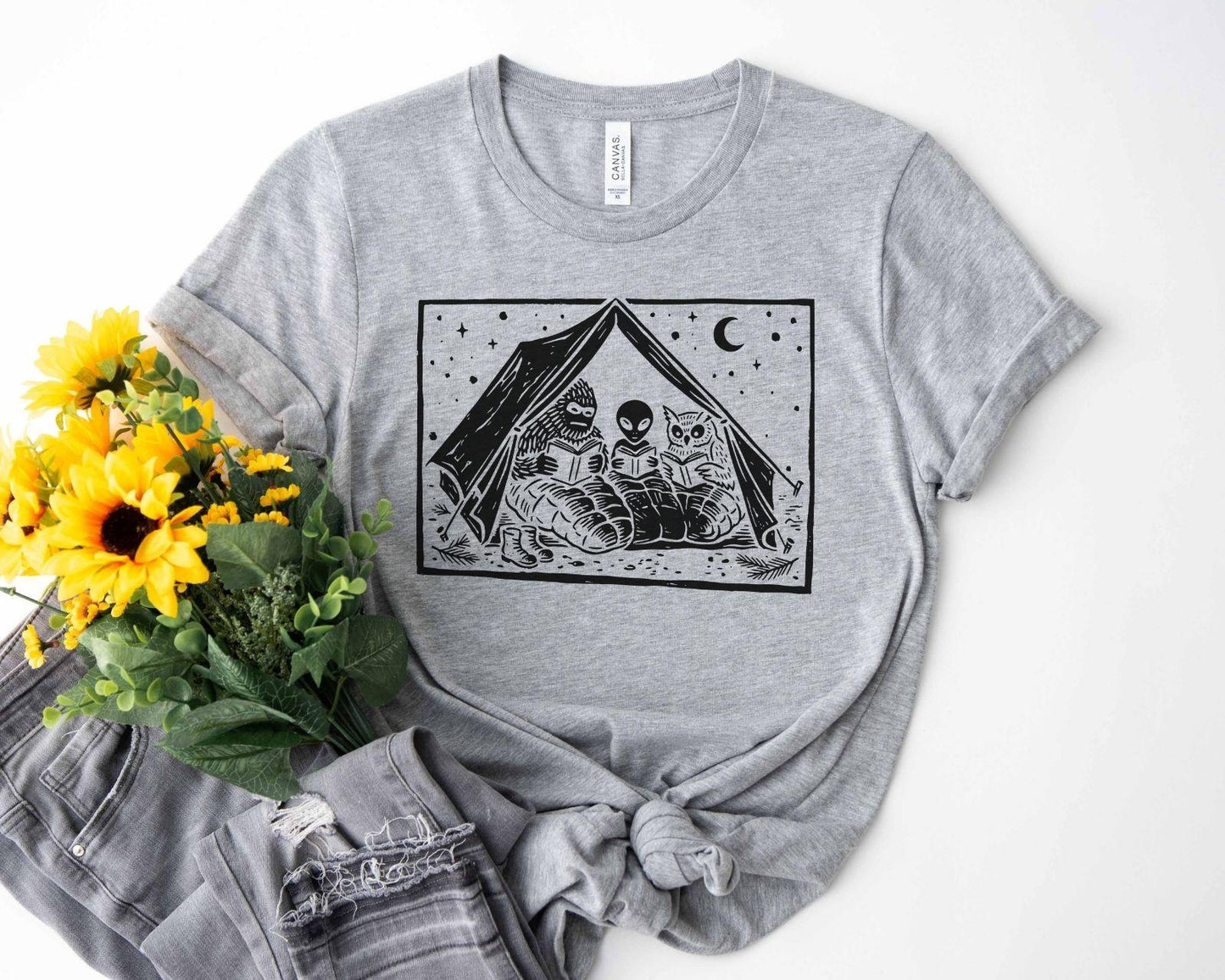 A bella canvas 3001 shirt with the saying "mothman, bigfoot and horned reading books"