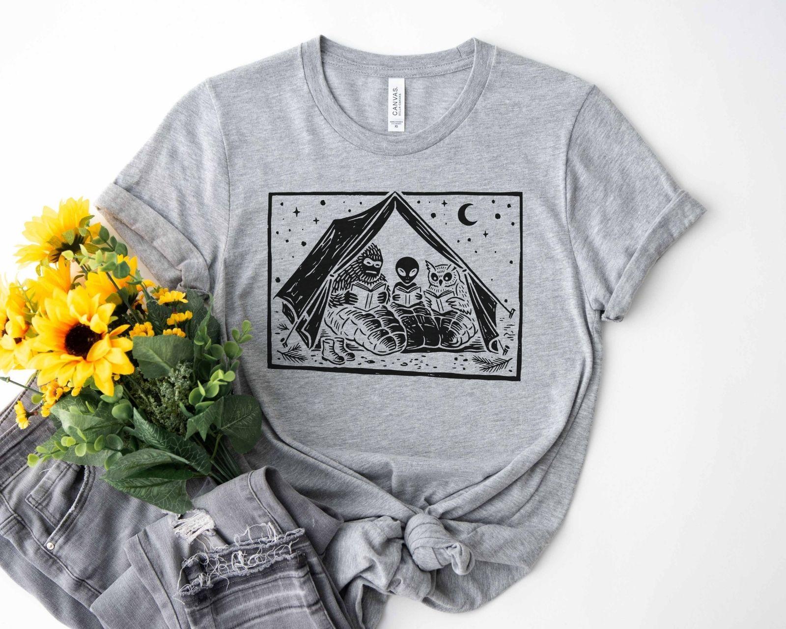 A bella canvas 3001 shirt with the saying "mothman, bigfoot and horned reading books"