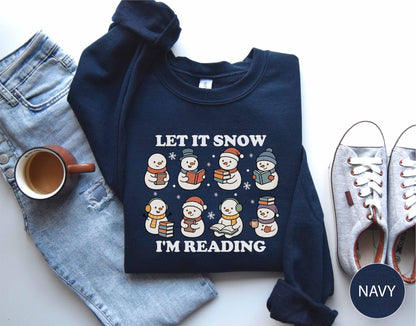 Navy sweatshirt with snowman design and text 'Let it Snow I'm Reading' on a white surface with jeans, mug, and shoes.