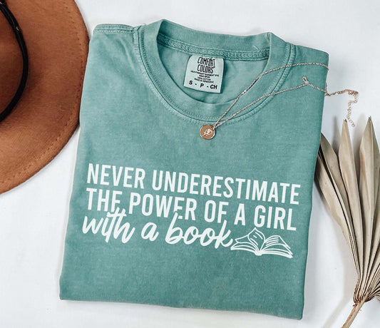 A comfort colors® shirt with the saying "Never underestimate the power of a girl with a book"