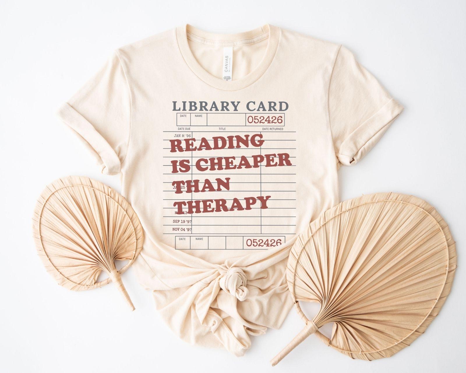 A bella canvas 3001 shirt with the saying "Reading is cheaper than therapy"