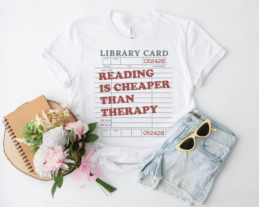A bella canvas 3001 shirt with the saying "Reading is cheaper than therapy"