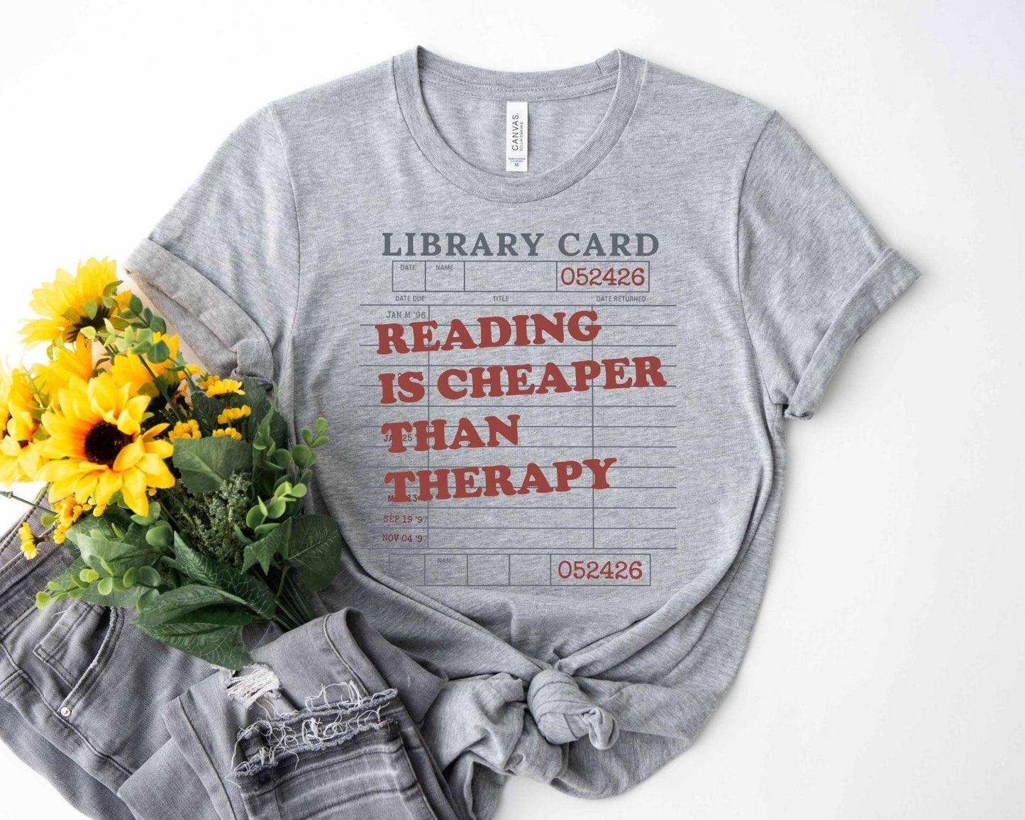 A bella canvas 3001 shirt with the saying "Reading is cheaper than therapy"