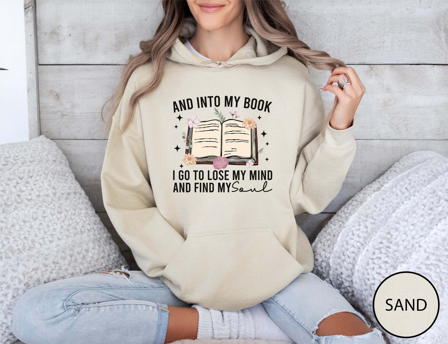 Person wearing a sand hoodie with a book-themed design, sitting on a couch.