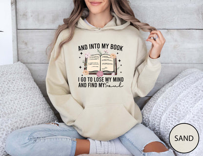 Person wearing a sand hoodie with a book-themed design, sitting on a couch.