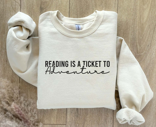 A sand color sweatshirt with the saying "Reading is a ticket to adventure"