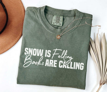 A comfort colors® shirt with the saying "Snow is falling books are calling"