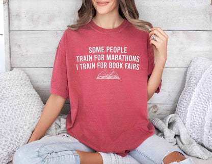 A comfort colors® shirt with the saying "some people train for marathons i train for book fairs"