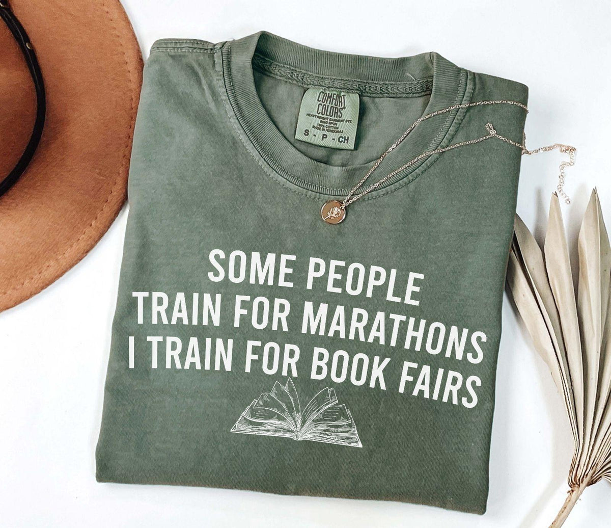 A comfort colors® shirt with the saying "some people train for marathons i train for book fairs"