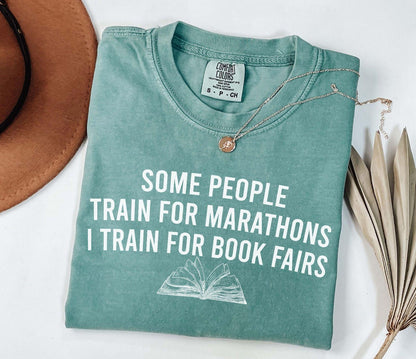 A comfort colors® shirt with the saying "some people train for marathons i train for book fairs"