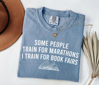 A comfort colors® shirt with the saying "some people train for marathons i train for book fairs"