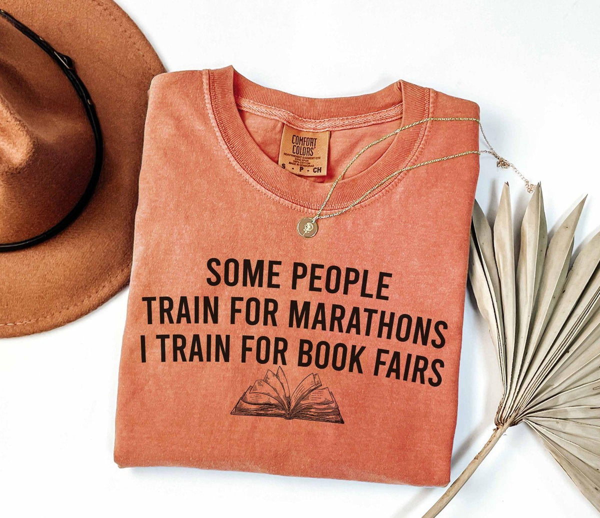 A comfort colors® shirt with the saying "some people train for marathons i train for book fairs"