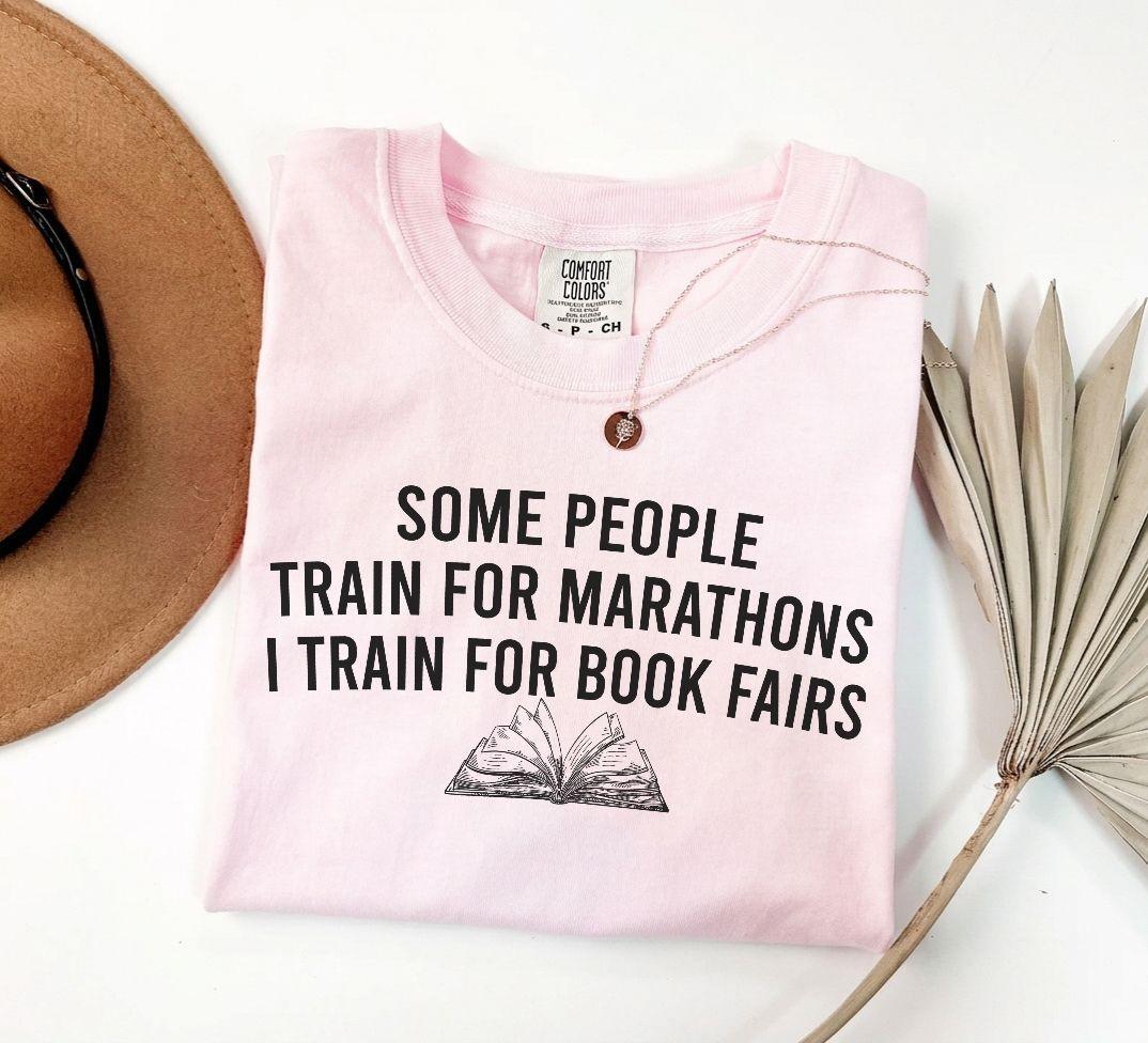 A comfort colors® shirt with the saying "some people train for marathons i train for book fairs"