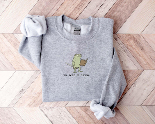 A Gildan 18000 sweatshirt with the saying "we read at dawn"