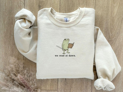 A Gildan 18000 sweatshirt with the saying "we read at dawn"