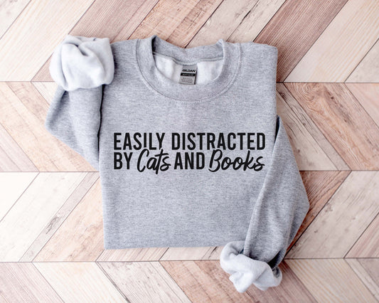 A sport grey color sweatshirt with the saying "Easily distracted by cats and books"