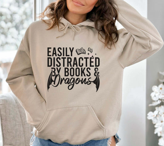 A sand color hoodie with the saying "Easily Distracted By Books And Dragons"